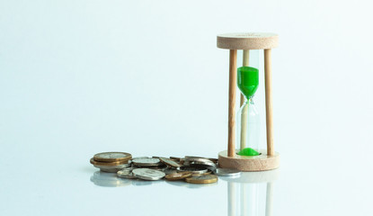 hourglass and coins on a white background and reflection in a mirror surface.