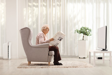 Elderly lady reading a newspaper in front of a tv