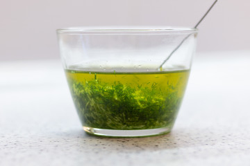 Glass bowl with spoon of sauce made of olive oil, garlic, dill on white marble table