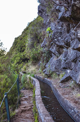 Fototapeta na wymiar Levada 25 Fontes in Madeira island, Portugal. Irrigation system canal, hiking path, green trees and rocks. Popular tourist attraction, hiking destination. Portuguese landscape. Trekking.