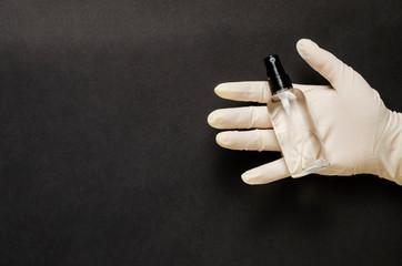 Naklejka premium Hand sanitizer bottle in gloved hand closeup on black background. Antibacterial liquid against 19-ncov.Call for hand disinfection. Using antibacterial gel for hands during quarantine.