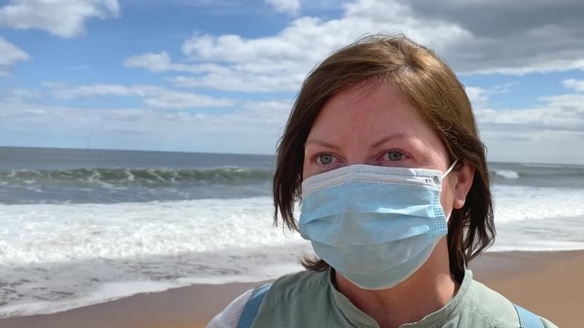 Pretty woman wearing a protective facemark on the beach during the covid19 - Coronavirus Pandemic. The new normal for tourism and holidays.