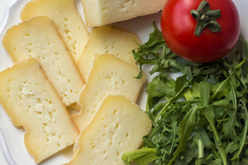 Cheese slices with tomato and arugula on plate