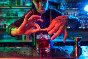 Close up of professional barman finishes preparation of alcoholic cocktail in multicolored neon...