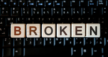Broken - concept text on wooden cubes on background black keyboard
