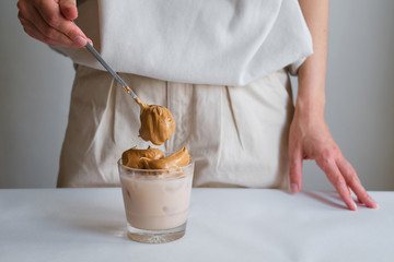 Dalgona coffee. Cold drink with ice. Whisk instant coffee, sugar and add in milk. Glass of coffee in girl hand. Woman barista making delicious summer beverage. Professional service