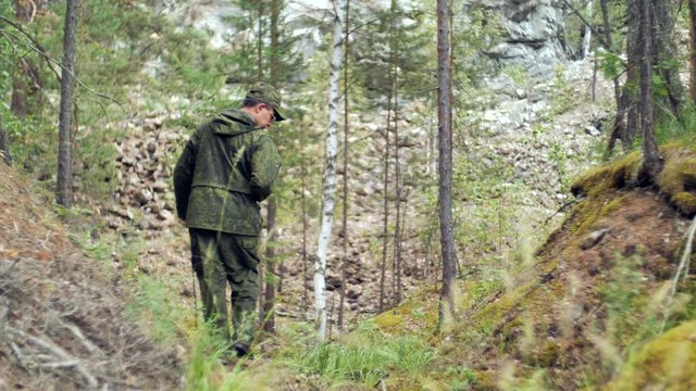 Forester in the reserve. A hunter in camouflage is walking through the forest. A man in green protective clothing is walking through the forest. Tourist in the wild. Man in nature.