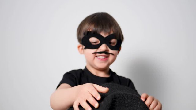 boy superhero in a black mask is trying to catch a hat flying in him