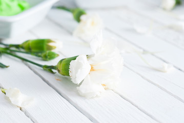 night cream with white carnation flowers on bright wooden table background