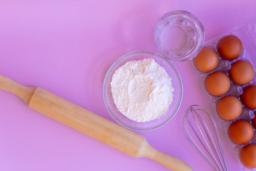 Products for the preparation of dough. Eggs, flour, water, whisk, rolling pin. Pink background