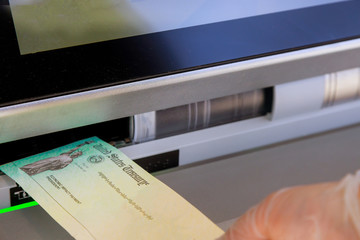 Hand of a woman with a deposit stimulus check in banking using an ATM