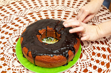 Hands slicing delicious and healthy traditional Brazilian homemade carrot cake with chocolate sauce. Top view. Copy space. Background with crochet towel.