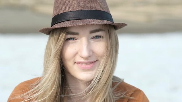 Portrait of a close-up Caucasian woman in casual clothes in a hat. The girl looks at the camera takes photos on a vintage camera and laughs merrily. Traveling with a camera along a deserted sea coast