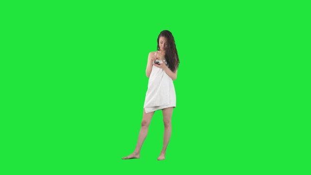 Frustrated young woman wrapped in towel using cell phone messaging displeased. Full body isolated on green screen background. 