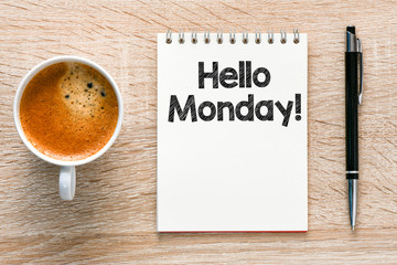 Hello Monday words written in a notebook on a wooden table.