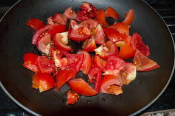 Cut the fresh red tomatoes into small pieces in a frying pan. Black background