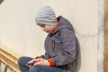 A European boy, a teenager in a blue jacket, writes a text message on his mobile phone in spring or autumn.