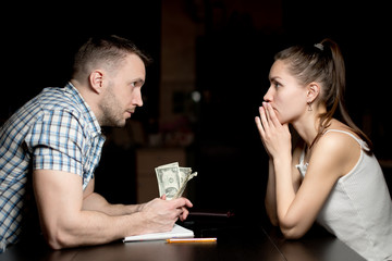 man and woman look at each other late at night, a man holding savings in dollars