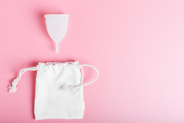 Reusable white menstrual cup and cotton eco bag on a pink background. Ecology and recycling concept, zero waste. Women's hygiene, menstruation, critical days.