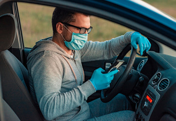 Beautiful young man sitting in a car, protective mask against coronavirus, wears medical gloves. Self-isolation and protection mode