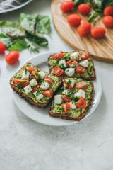 Bruschetta toast with guacamole and tomatoes, sea salt and herbs on dark bread and a white plate, healthy nutrition.