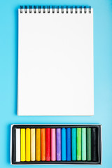 colorful pastel and white blank notebook on a blue background. Concept of drawing course for children and adult. Copy space, flat lay, mockup.