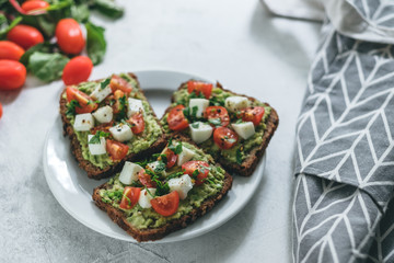 Bruschetta toast with guacamole and tomatoes, sea salt and herbs on dark bread and a white plate, healthy nutrition.