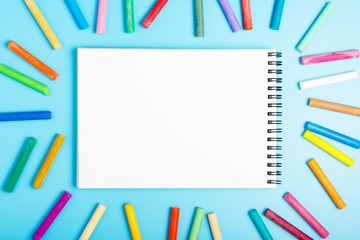 frame of color pastel and white blank notebook on a blue background. Concept of drawing course for children. Copy space, flat lay, mockup.