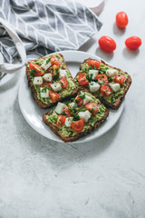 Bruschetta toast with guacamole and tomatoes, sea salt and herbs on dark bread and a white plate, healthy nutrition.