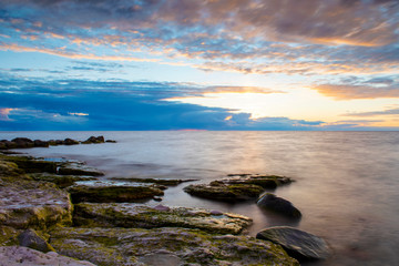 Obraz premium sunset storm clouds over ocean with boulders in foreground