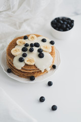 Pancakes with condensed milk with fresh blueberries and banana in a white plate on a white background.
