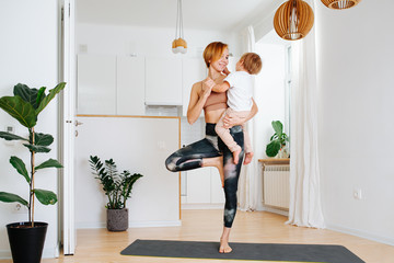 Mother doing yoga while holding her little son, giving attention to him.
