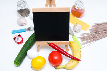 Copy space. Slate, tomatoes, banana, red paper, lemon, egg, fork, clock, knife, pasta, garlic, spices and cucumber on white background. Cooking at home. Cooking. Kitchen utensils. 