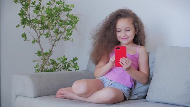 Curious cute boy preschool child using a digital tablet technology device looks telephone.Plays in the phone sitting on the sofa alone.Children tech addiction concept play game at home.