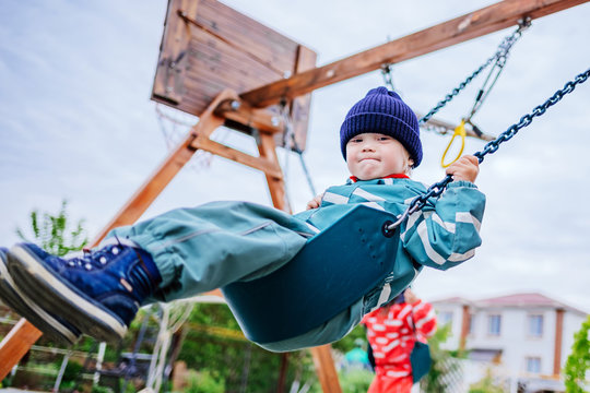 A boy with Down syndrome plays on the playground, he is swinging on a swing. Genetic disease in a child.