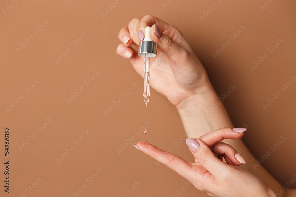 Wall mural hands of cropped white woman holding cosmetic serum pipette on the orange background.