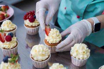 Confectioner decorate cupcakes with cream cheese and berries, close up.