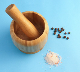 Wooden mortar and pestle next to black pepper and sea salt on a blue background