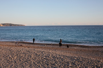 people walking and fishing on the beach, sunset in Nice, France