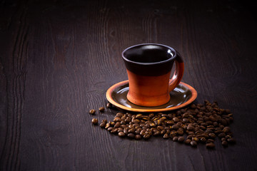 Brown clay coffee cup and saucer on a dark background with coffee beans.