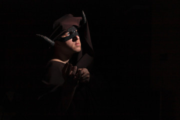 A man with twisted horns in a dark cape, mask and turban depicts a demon on a dark background with copyspace