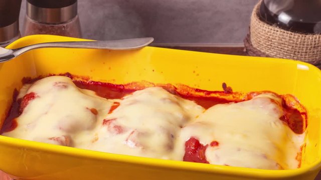Delicious Chicken Parmigiana served in yellow baking dish wtih smoke on a wooden table and stone or concrete background