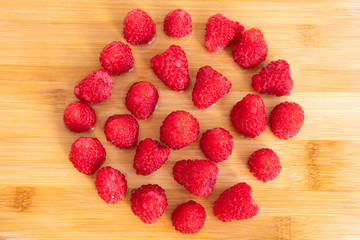 Fresh red raspberry fruits alined in a circle on wooden chopping board. Healthy Selective focus. Berry with antioxidants, Vitamin C