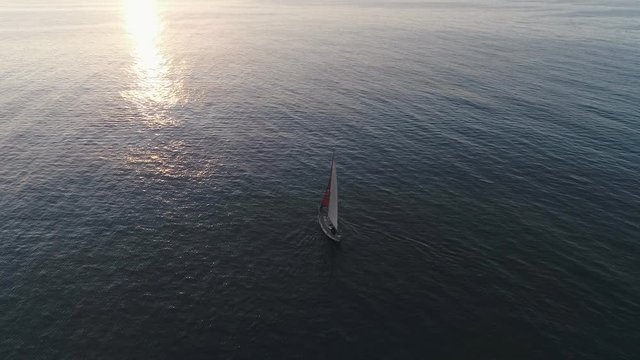 AERIAL DRONE TILT-UP OF SAIL BOAT IN A CALM BLUE SEA WITH SUNSET