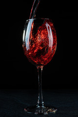 Wine. Red wine pouring into a wine glass. Isolated on black background.
