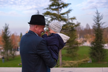 great-grandfather and great-grandson. the grandfather holds the grandson in his arms. happiness joy blue color. black hat. two