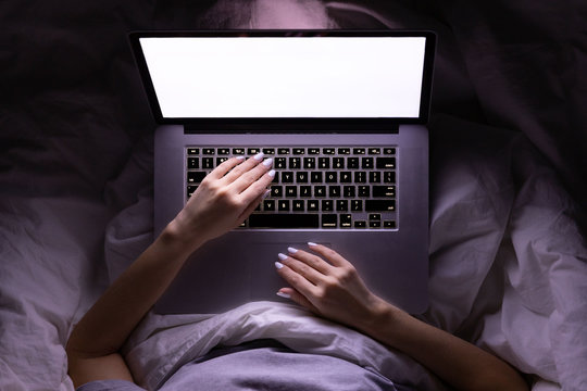 Woman in glasses lying in bed covered by blanket and working on laptop late at night, can not sleep, news search or sharing social media. Insomnia, freelance job, melatonin. Top view. 