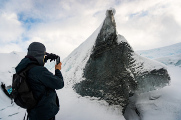 Fototapeta na wymiar Adventurer hiker taking a picture of a rock, piece of ice with the shape of a wolf / dog raising from the snow in Matanuska Glacier, Anchorage, Alaska. It's the call of the wild. 