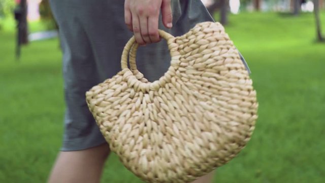 Young woman with handmade stylish straw handbag walks in the summer park. Eco bag.
