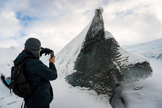 Adventurer hiker taking a picture of a rock, piece of ice with the shape of a wolf / dog raising from the snow in Matanuska Glacier, Anchorage, Alaska. It's the call of the wild. 